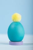 Uovo di Pasqua luminoso tinto in un supporto con il fiocchetto variopinto su un fondo blu fotografie stock Uovo di Pasqua luminoso tinto in un supporto con il fiocchetto variopinto su un fondo blu fotografie stock
