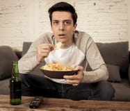 Upphetsad och lycklig ung man som sitter på den hållande ögonen på TV:N för soffa TV som programmerar begrepp arkivbilder Upphetsad och lycklig ung man som sitter på den hållande ögonen på TV:N för soffa TV som programmerar begrepp arkivbilder