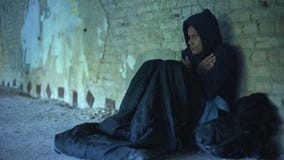 Upset homeless teenager wearing hoodie, people passing by indifferently, poverty