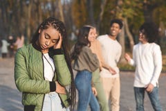 Upset Teen Black Girl With Friends Gossiping In Background Stock Photo