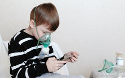 Use nebulizer and inhaler for the treatment. Boy inhaling through inhaler mask and playing the game in his mobile phone royalty free stock photography Use nebulizer and inhaler for the treatment. Boy inhaling through inhaler mask and playing the game in his mobile phone royalty free stock photography