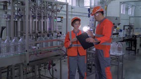 Usine de production, ingénieurs forts de fille et de type dans les casques et vêtements de travail avec l'ordinateur portable de banque de vidéos Usine de production, ingénieurs forts de fille et de type dans les casques et vêtements de travail avec l'ordinateur portable de banque de vidéos