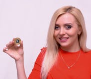 Uśmiechnięta blondynki dziewczyna w czerwieni sukni chwyta złotym bitcoin w dwa palcach obrazy royalty free Uśmiechnięta blondynki dziewczyna w czerwieni sukni chwyta złotym bitcoin w dwa palcach obrazy royalty free