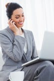 Uśmiechnięty bizneswoman dzwoni z jej telefonem komórkowym i używa laptopu obsiadanie na kanapie Fotografia Royalty Free Uśmiechnięty bizneswoman dzwoni z jej telefonem komórkowym i używa laptopu obsiadanie na kanapie Fotografia Royalty Free
