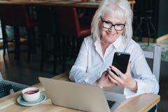 Uśmiechnięty bizneswoman ubierający w białej koszula siedzi przy stołem przed laptopem i używa smartphone freelancer Fotografia Royalty Free Uśmiechnięty bizneswoman ubierający w białej koszula siedzi przy stołem przed laptopem i używa smartphone freelancer Fotografia Royalty Free