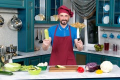 Uśmiechnięty Cook z nożem i zieleni zuccini w rękach Mężczyzna ` s główna broń przy kuchnią obraz royalty free Uśmiechnięty Cook z nożem i zieleni zuccini w rękach Mężczyzna ` s główna broń przy kuchnią obraz royalty free