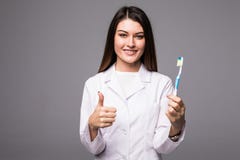 Uśmiechnięty kobieta dentysta pokazuje toothbrush, odizolowywającego nad popielatym tłem Młodej atrakcyjnej stomatologicznej klin zdjęcia stock Uśmiechnięty kobieta dentysta pokazuje toothbrush, odizolowywającego nad popielatym tłem Młodej atrakcyjnej stomatologicznej klin zdjęcia stock
