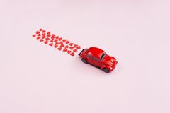 Valentine\'s Day background. Red retro toy car  red hearts confetti  on pink background. Valentines day creative concept.