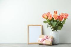 Vase avec les roses, le cadeau et le cadre vide sur la table grise sur le fond blanc images libres de droits Vase avec les roses, le cadeau et le cadre vide sur la table grise sur le fond blanc images libres de droits