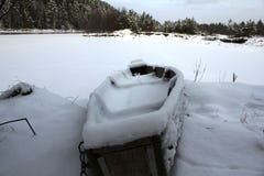 Vecchia barca innevata sulla banca di un fiume congelato immagine stock Vecchia barca innevata sulla banca di un fiume congelato immagine stock