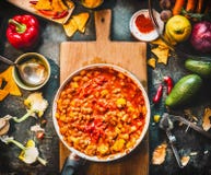 Vegetarian chili con carne dish in pan on wooden cutting board with spices and vegetables cooking ingredients on dark kitchen tabl Royalty Free Stock Photo Vegetarian chili con carne dish in pan on wooden cutting board with spices and vegetables cooking ingredients on dark kitchen tabl Royalty Free Stock Photo