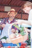 Venda de fazendeiro madura feliz seus vegetais orgânicos frescos em um mercado imagens de stock Venda de fazendeiro madura feliz seus vegetais orgânicos frescos em um mercado imagens de stock