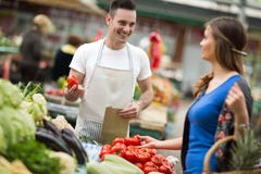 Vendedor novo que sorri e que guarda vegetal no mercado foto de stock Vendedor novo que sorri e que guarda vegetal no mercado foto de stock