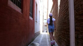 VENEZA, ITÁLIA - 7 DE JULHO DE 2018: ao longo de uma rua estreita de Veneza, entre casas velhas, uma menina do adolescente, uma c vídeos de arquivo VENEZA, ITÁLIA - 7 DE JULHO DE 2018: ao longo de uma rua estreita de Veneza, entre casas velhas, uma menina do adolescente, uma c vídeos de arquivo