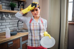 Vermoeide vrouwelijke schonere tribune in keuken en greephand op voorhoofd Zij draagt schort en gele handschoenen Het wit van de royalty-vrije stock afbeeldingen Vermoeide vrouwelijke schonere tribune in keuken en greephand op voorhoofd Zij draagt schort en gele handschoenen Het wit van de royalty-vrije stock afbeeldingen