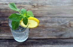Verre avec de l'eau froid scintillement, une tranche d'un citron et verts frais de minute Images libres de droits Verre avec de l'eau froid scintillement, une tranche d'un citron et verts frais de minute Images libres de droits