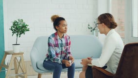 Verstoor jonge dame in toevallige kleding heeft therapiezitting met psycholoog in lichte studio Het meisje spreekt en stock footage Verstoor jonge dame in toevallige kleding heeft therapiezitting met psycholoog in lichte studio Het meisje spreekt en stock footage