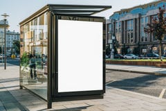 Vertical blank billboard at bus stop on city street. In background buildings, road. Mock up. Poster next to roadway.