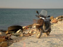 Vespa de motor vieja en la orilla rocosa de la bahía amplia del mar por la tarde en el resplandor caliente del sol poniente fotos de archivo Vespa de motor vieja en la orilla rocosa de la bahía amplia del mar por la tarde en el resplandor caliente del sol poniente fotos de archivo