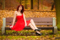 Vestido rojo de la mujer que se sienta en banco en parque del otoño Imágenes de archivo libres de regalías Vestido rojo de la mujer que se sienta en banco en parque del otoño Imágenes de archivo libres de regalías