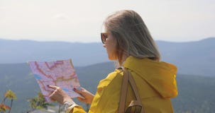 Viandante in un impermeabile giallo che esamina mappa dalla cima della montagna donna con la mappa in montagne 4k stock footage Viandante in un impermeabile giallo che esamina mappa dalla cima della montagna donna con la mappa in montagne 4k stock footage