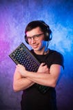 Videojugador profesional del muchacho que sostiene el teclado del juego sobre rosa colorido y la pared encendida de neón azul Con fotografía de archivo libre de regalías Videojugador profesional del muchacho que sostiene el teclado del juego sobre rosa colorido y la pared encendida de neón azul Con fotografía de archivo libre de regalías
