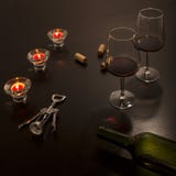 Vidros de vinho em uma tabela com uma garrafa vazia, um corkscrew e cortiça da garrafa nos tons escuros iluminados por diversas v foto de stock royalty free Vidros de vinho em uma tabela com uma garrafa vazia, um corkscrew e cortiça da garrafa nos tons escuros iluminados por diversas v foto de stock royalty free