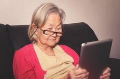 Vidros vestindo da mulher adulta em casa que leem algo tabuleta imagem de stock Vidros vestindo da mulher adulta em casa que leem algo tabuleta imagem de stock