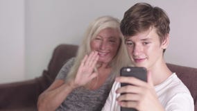 Vieille grand-mère et petit-fils adulte employant l'application mobile sur le tougether de téléphone asseyant sur le sofa Faire l banque de vidéos Vieille grand-mère et petit-fils adulte employant l'application mobile sur le tougether de téléphone asseyant sur le sofa Faire l banque de vidéos