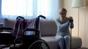 Vieille veuve bouleversée s'asseyant sur le sofa, mari absent, fauteuil roulant vide dans la chambre photo stock Vieille veuve bouleversée s'asseyant sur le sofa, mari absent, fauteuil roulant vide dans la chambre photo stock