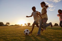 Vier kinderen die na een voetbal rennen die op een gebied beoefenen stock foto's Vier kinderen die na een voetbal rennen die op een gebied beoefenen stock foto's