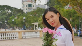 Vietnam girl in the national costume and dress Ao Dai posing and smiling for the camera. In the hands holding a pink