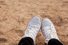 View of the legs in white sneakers on background of shell beach. Atmospheric, melancholic mood, blurred background with copy space royalty free stock photography View of the legs in white sneakers on background of shell beach. Atmospheric, melancholic mood, blurred background with copy space royalty free stock photography