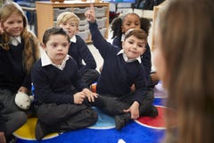 View over female teacher`s shoulder of primary school kids sitting on the floor in the classroom stock image View over female teacher`s shoulder of primary school kids sitting on the floor in the classroom stock image