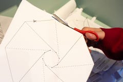 View of a woman`s hand cutting a marked paper with a pair of scissors to make an origami craft