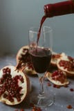Vinho tinto com uma romã aberta em um fundo concreto cinzento textured Um homem derrama o vinho tinto de uma garrafa foto de stock Vinho tinto com uma romã aberta em um fundo concreto cinzento textured Um homem derrama o vinho tinto de uma garrafa foto de stock