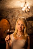 Vinho tinto louro novo bonito do gosto da mulher em uma adega de vinho fotografia de stock Vinho tinto louro novo bonito do gosto da mulher em uma adega de vinho fotografia de stock