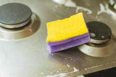 Violett - gelber Schwamm mit einem Metall-Gasofen Säubern des Schmutzes mit einem Schwamm mit Schaum lizenzfreie stockfotos Violett - gelber Schwamm mit einem Metall-Gasofen Säubern des Schmutzes mit einem Schwamm mit Schaum lizenzfreie stockfotos
