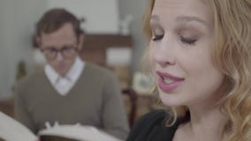 Visage en gros plan de la belle femme blonde lisant à haute voix le livre dans le premier plan tandis qu'homme modestement habill banque de vidéos Visage en gros plan de la belle femme blonde lisant à haute voix le livre dans le premier plan tandis qu'homme modestement habill banque de vidéos