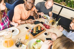 Visi?n superior Una compa??a de la gente joven de la compa??a multicultural en un caf? que come los rollos de sushi, bebidas de c foto de archivo libre de regalías Visi?n superior Una compa??a de la gente joven de la compa??a multicultural en un caf? que come los rollos de sushi, bebidas de c foto de archivo libre de regalías