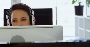 Vista frontale della donna di affari caucasica in cuffie che lavorano al computer allo scrittorio in ufficio 4k stock footage Vista frontale della donna di affari caucasica in cuffie che lavorano al computer allo scrittorio in ufficio 4k stock footage