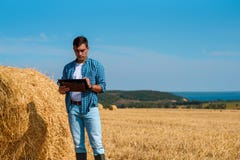 Vista frontale di un agricoltore maschio dell'agronomo con una compressa in blue jeans e una camicia e una maglietta bianca in un fotografia stock libera da diritti Vista frontale di un agricoltore maschio dell'agronomo con una compressa in blue jeans e una camicia e una maglietta bianca in un fotografia stock libera da diritti