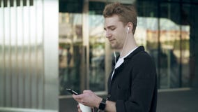 Vista lateral del hombre joven sonriente con smartphone y del café que escuchan la música almacen de video Vista lateral del hombre joven sonriente con smartphone y del café que escuchan la música almacen de video