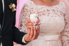 Vit stearinljus med en garnering av blommor i händerna av nygifta personerna Begreppet av familjhärden royaltyfri bild Vit stearinljus med en garnering av blommor i händerna av nygifta personerna Begreppet av familjhärden royaltyfri bild