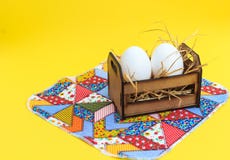 Vita ägg i en träspjällåda, på en patchworkfilt, med gul bakgrund fotografering för bildbyråer Vita ägg i en träspjällåda, på en patchworkfilt, med gul bakgrund fotografering för bildbyråer