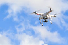 Vitt quadcoptersurr med kameran i en blå himmel arkivfoton Vitt quadcoptersurr med kameran i en blå himmel arkivfoton