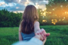 Volg me, Aantrekkelijk donkerbruin meisje die de hand van de lood op een schoon groen gebied met bomen houden bij zonsondergang stock afbeeldingen Volg me, Aantrekkelijk donkerbruin meisje die de hand van de lood op een schoon groen gebied met bomen houden bij zonsondergang stock afbeeldingen