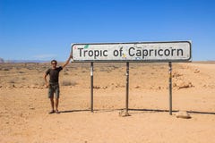 Voyageur masculin caucasien blanc dans la position de vêtements de sport à côté du signe tropical de Capricorne en parc national images stock Voyageur masculin caucasien blanc dans la position de vêtements de sport à côté du signe tropical de Capricorne en parc national images stock