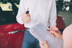 Vriendschappelijke autoverkoper die aan een jonge vrouw spreken en een nieuwe auto binnen toonzaal het Ondertekenen van contract stock foto Vriendschappelijke autoverkoper die aan een jonge vrouw spreken en een nieuwe auto binnen toonzaal het Ondertekenen van contract stock foto