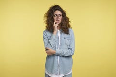 Vrij jonge vrouw in oogglazen denken aan iets en blikken een kant, geïsoleerd over gele achtergrond stock fotografie Vrij jonge vrouw in oogglazen denken aan iets en blikken een kant, geïsoleerd over gele achtergrond stock fotografie